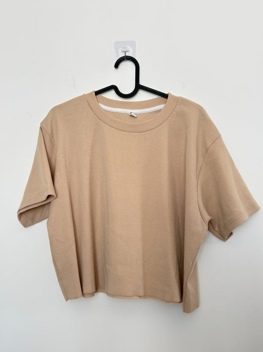 The Circle beige ribbed knit short sleeve boxy crop top with a crew neckline hanging on a black hanger.