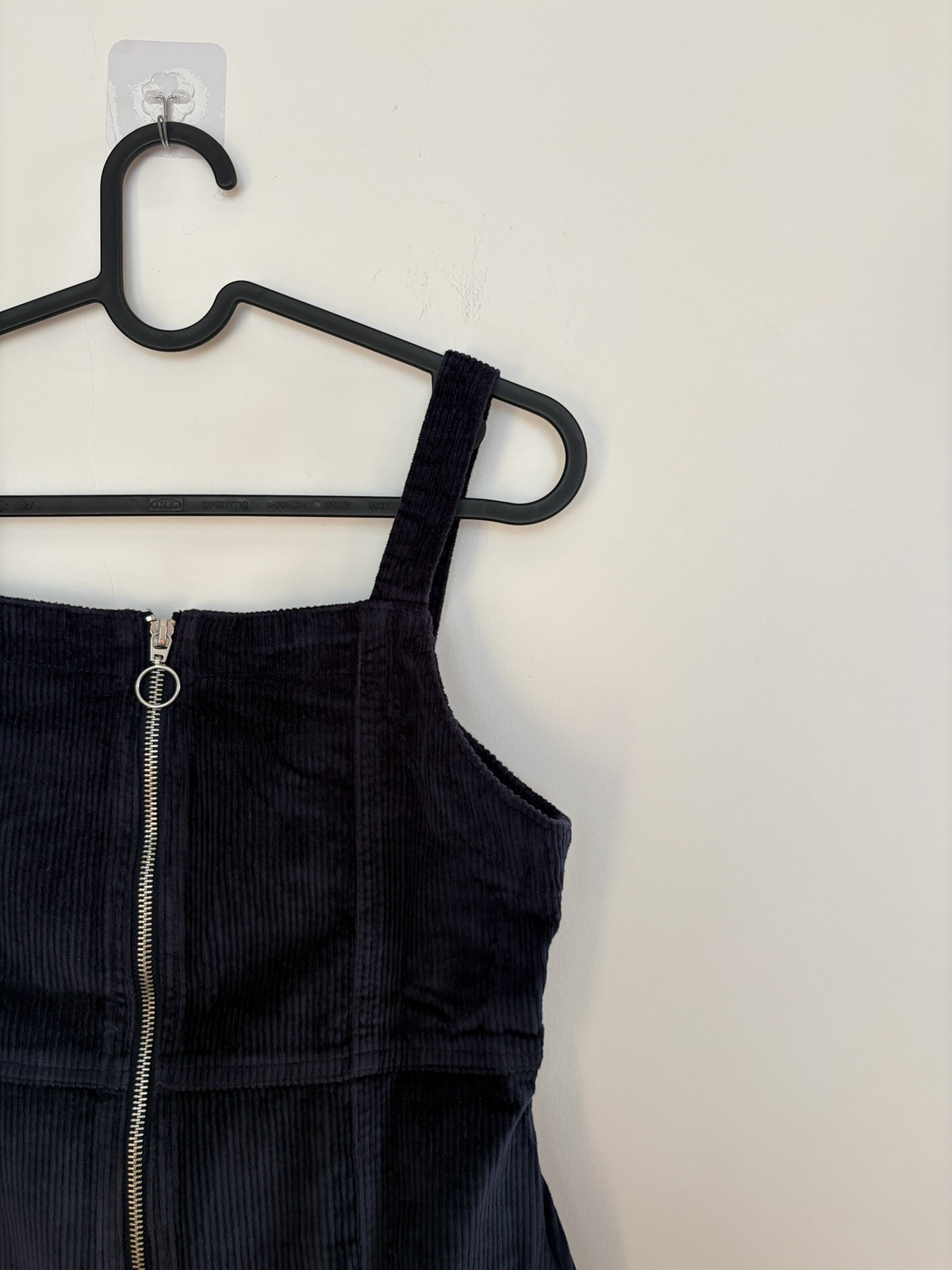 The Circle black corduroy pinafore dress featuring a square neckline and a silver front zipper with a ring pull.