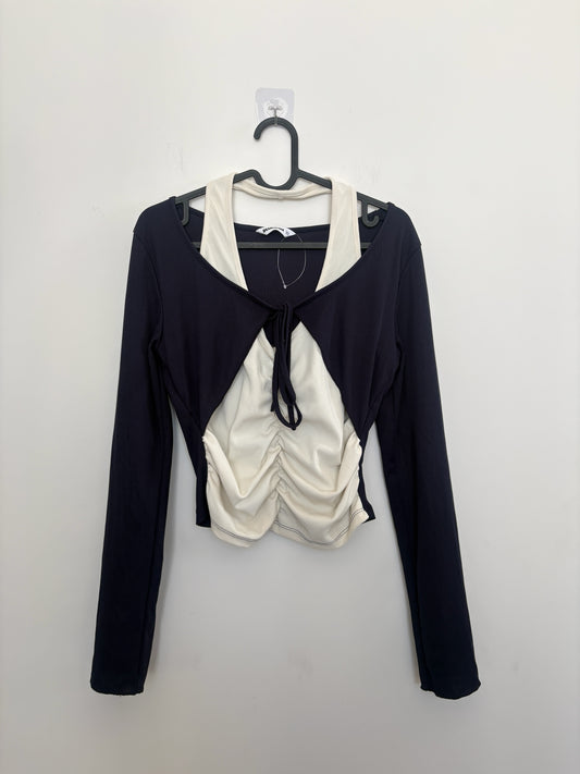 The Circle layered long sleeve crop top featuring a black shrug over a cream ruched tank with a front tie detail.