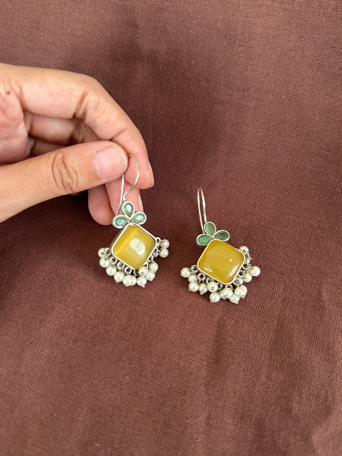 The Circle handcrafted silver-toned drop earrings featuring a square yellow stone, green floral motifs, and white pearls.