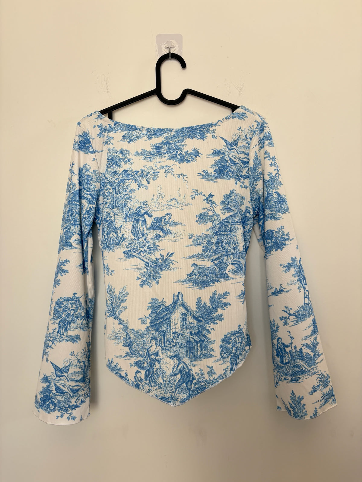 The Circle blue and white toile print long sleeve top with a sweetheart neckline and flared sleeves on a hanger.