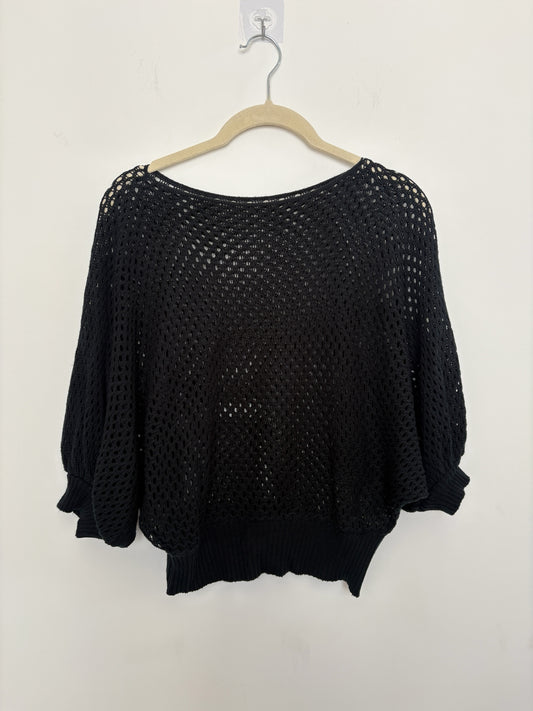 The Circle black open-knit pullover sweater with batwing sleeves and a ribbed hem hanging on a hanger.