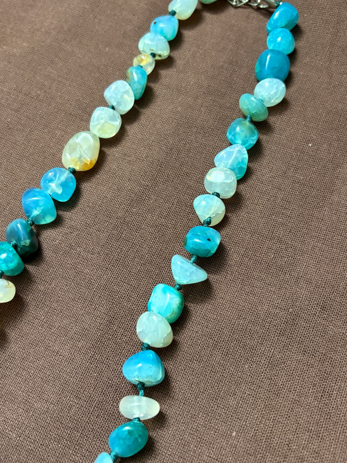 The Circle handcrafted necklace featuring polished blue agate gemstone beads on a knotted thread with a silver clasp.