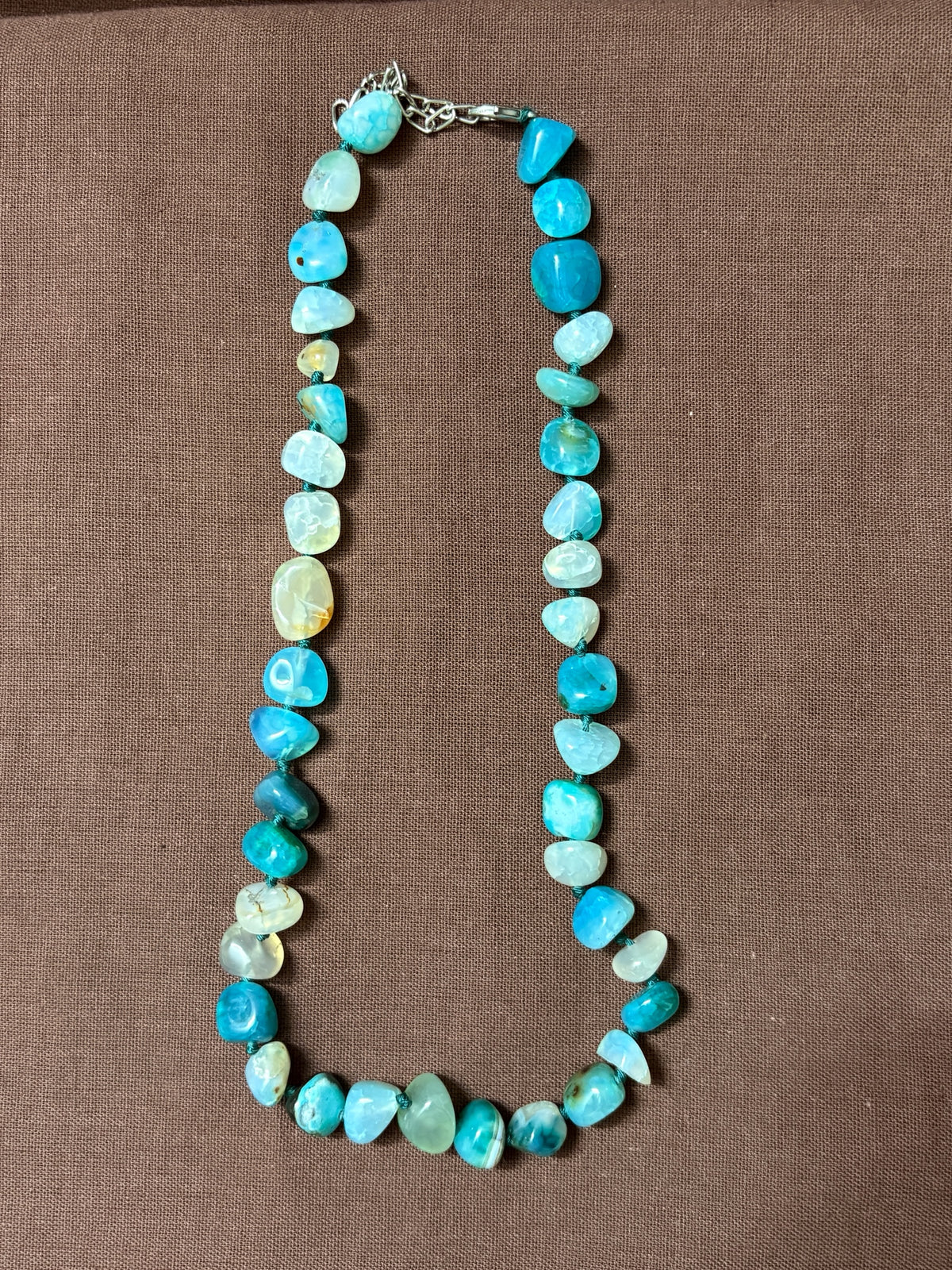 The Circle handcrafted necklace featuring polished blue agate gemstone beads in turquoise and aquamarine on a brown background.