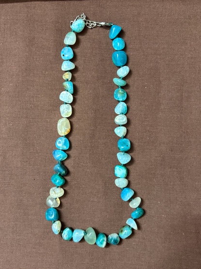 The Circle handcrafted necklace featuring polished blue agate gemstone beads in turquoise and aquamarine on a brown background.