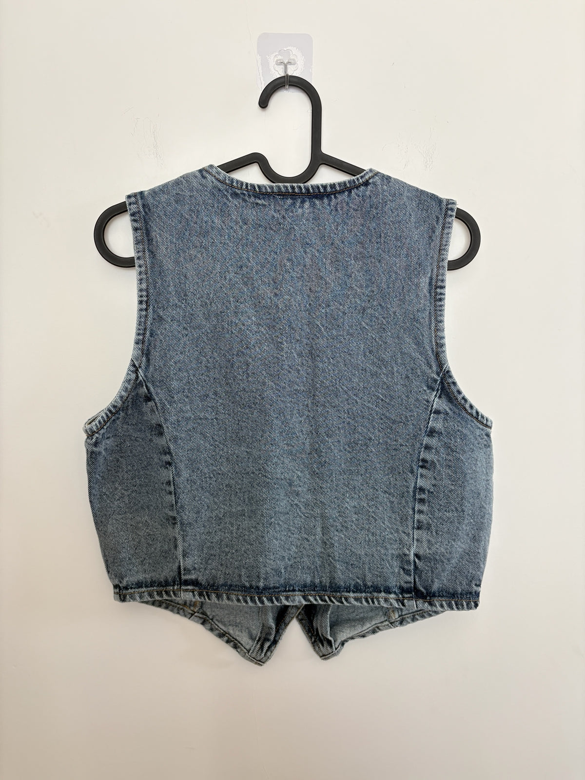 The Circle sleeveless washed-blue denim waistcoat featuring a tailored back view on a black hanger.