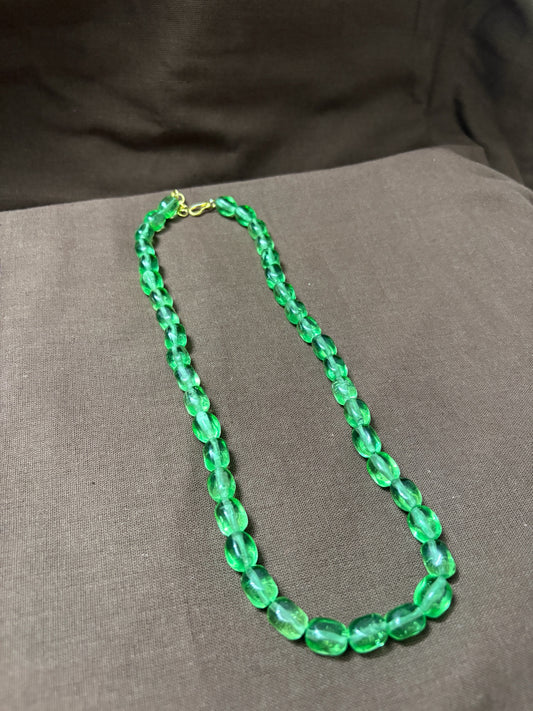 The Circle emerald-green translucent beaded necklace with a polished finish and gold-toned clasp on a brown background