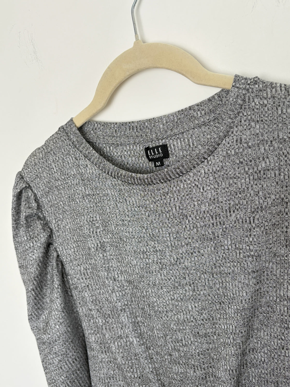 The Circle grey textured knit pullover top by ELLE STUDIO featuring a crew neckline and puff sleeves on a hanger.