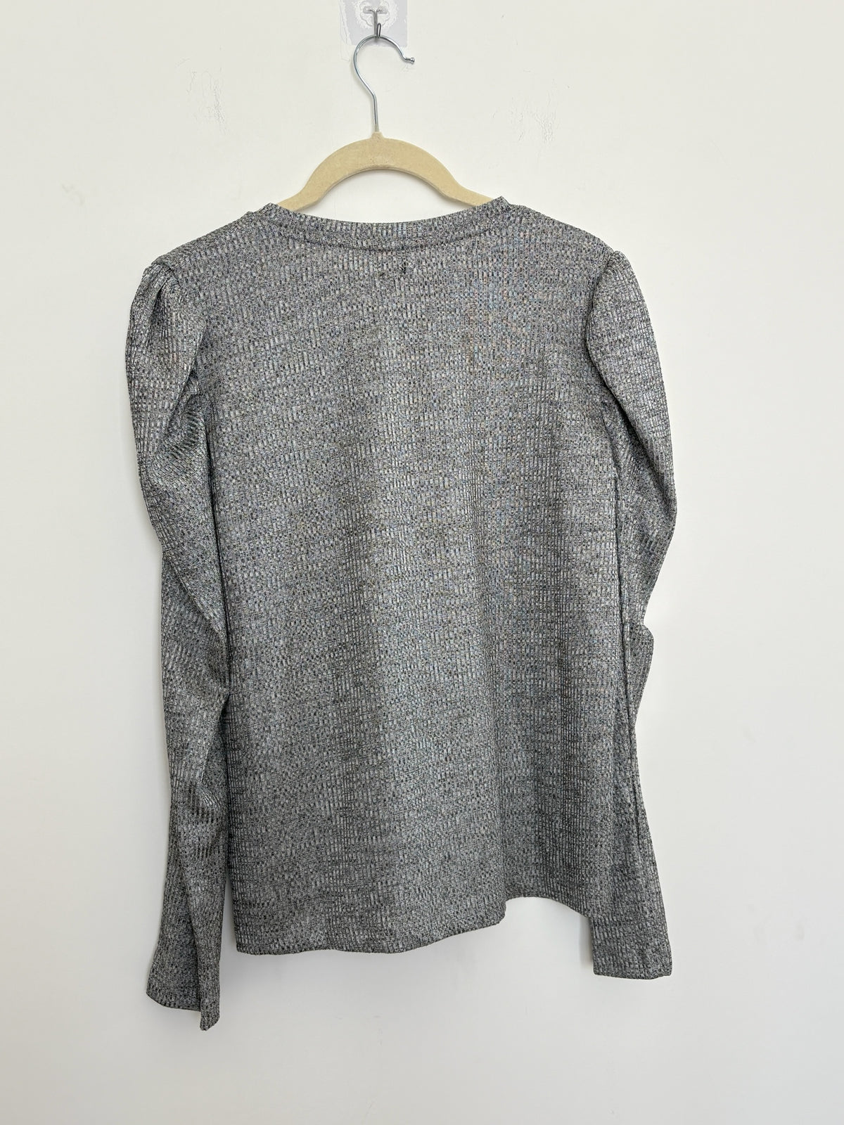 The Circle grey knit pullover top with long puff sleeves and a crew neckline hanging on a hanger against a white wall.