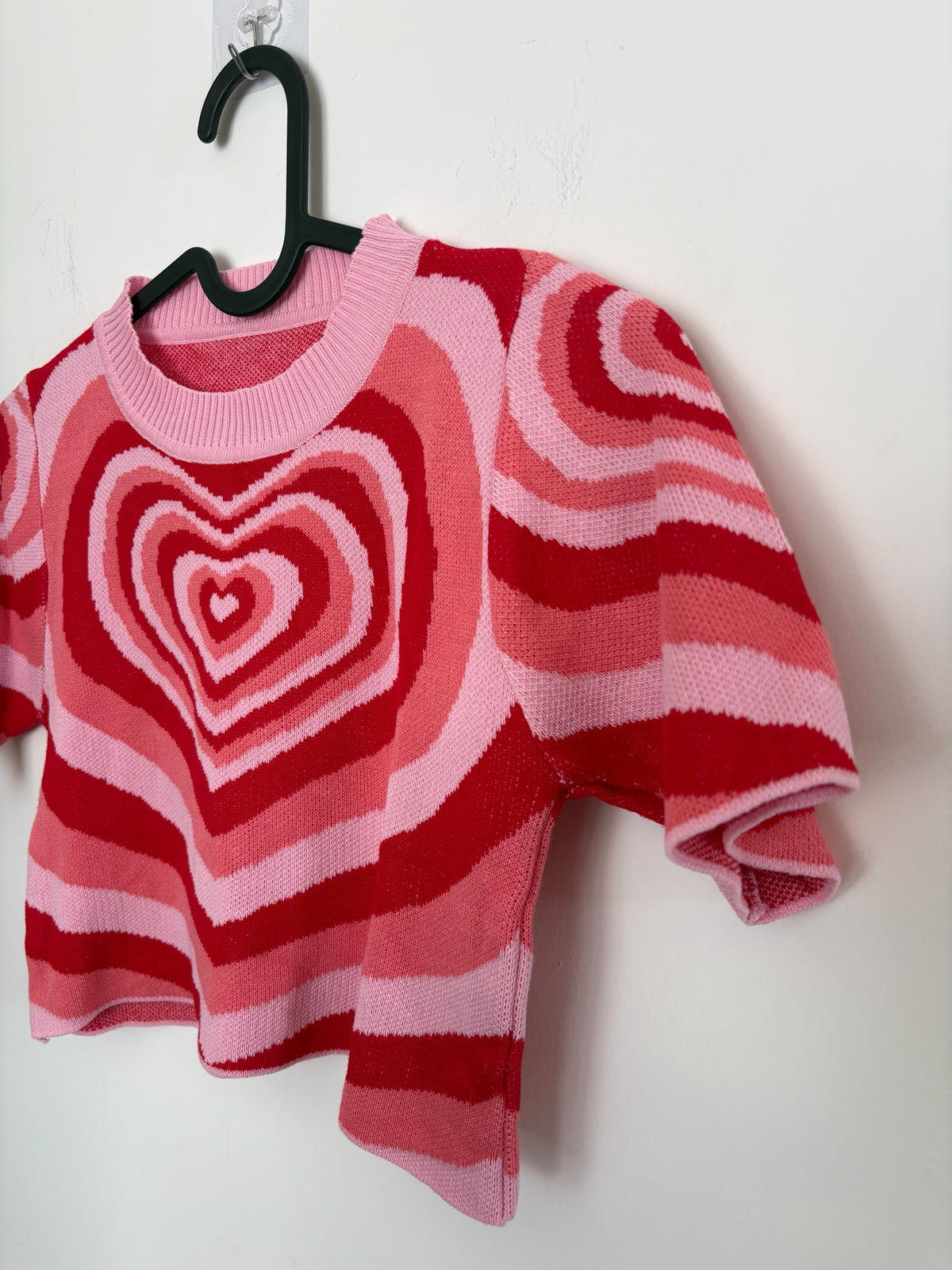 The Circle short sleeve knit crop top featuring a vibrant pink and red concentric heart pattern and crew neckline.