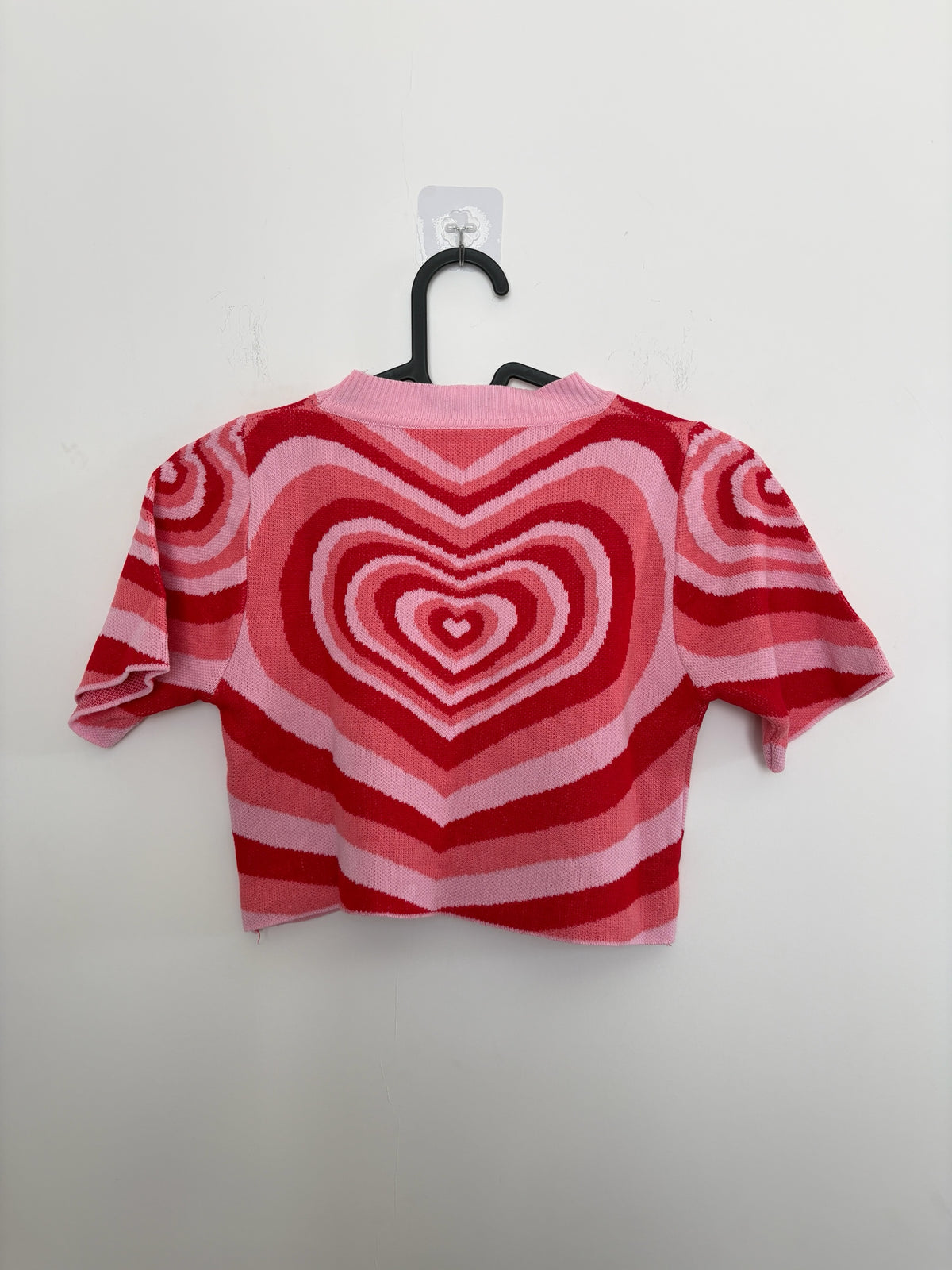 The Circle short sleeve knit crop top featuring a bold pink and red concentric heart pattern and ribbed crew neckline.