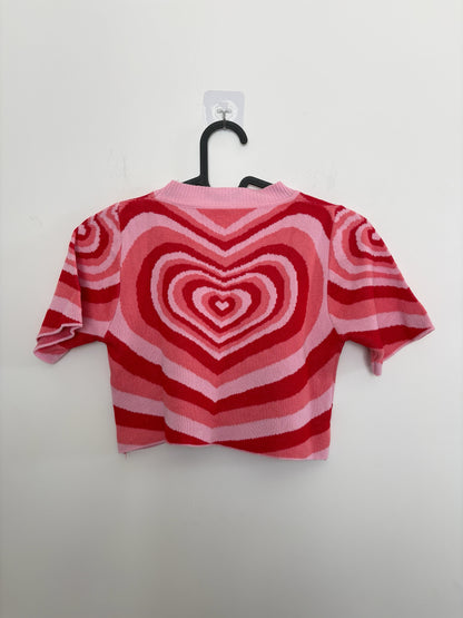 The Circle short sleeve knit crop top featuring a bold pink and red concentric heart pattern and ribbed crew neckline.