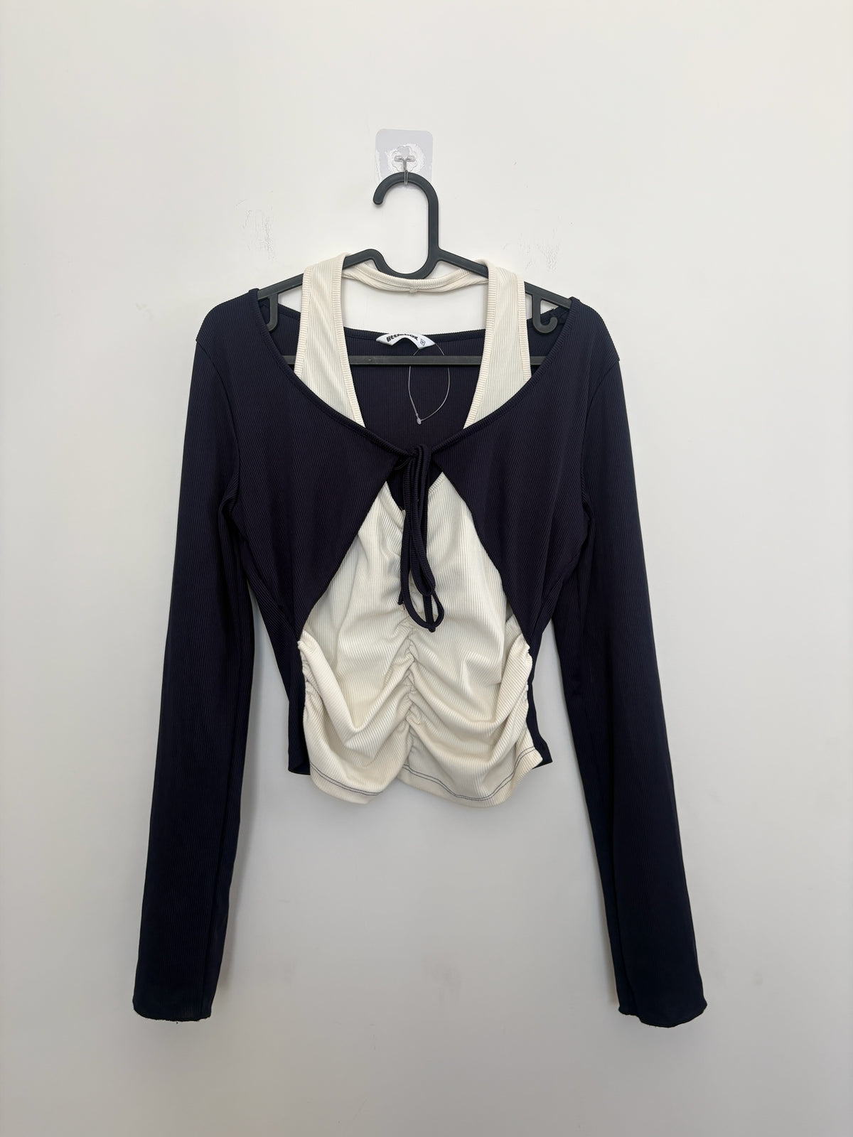 The Circle layered long sleeve crop top featuring a black shrug over a cream ruched tank with a front tie detail.