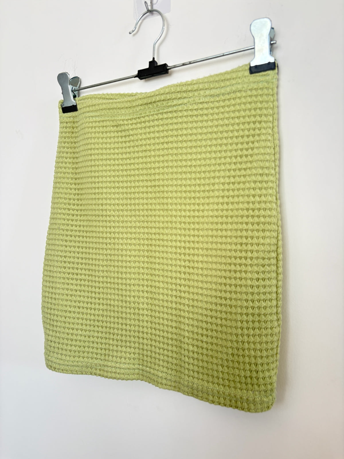The Circle lime green mini skirt in a textured waffle-knit fabric hanging on a metal hanger against a white wall.