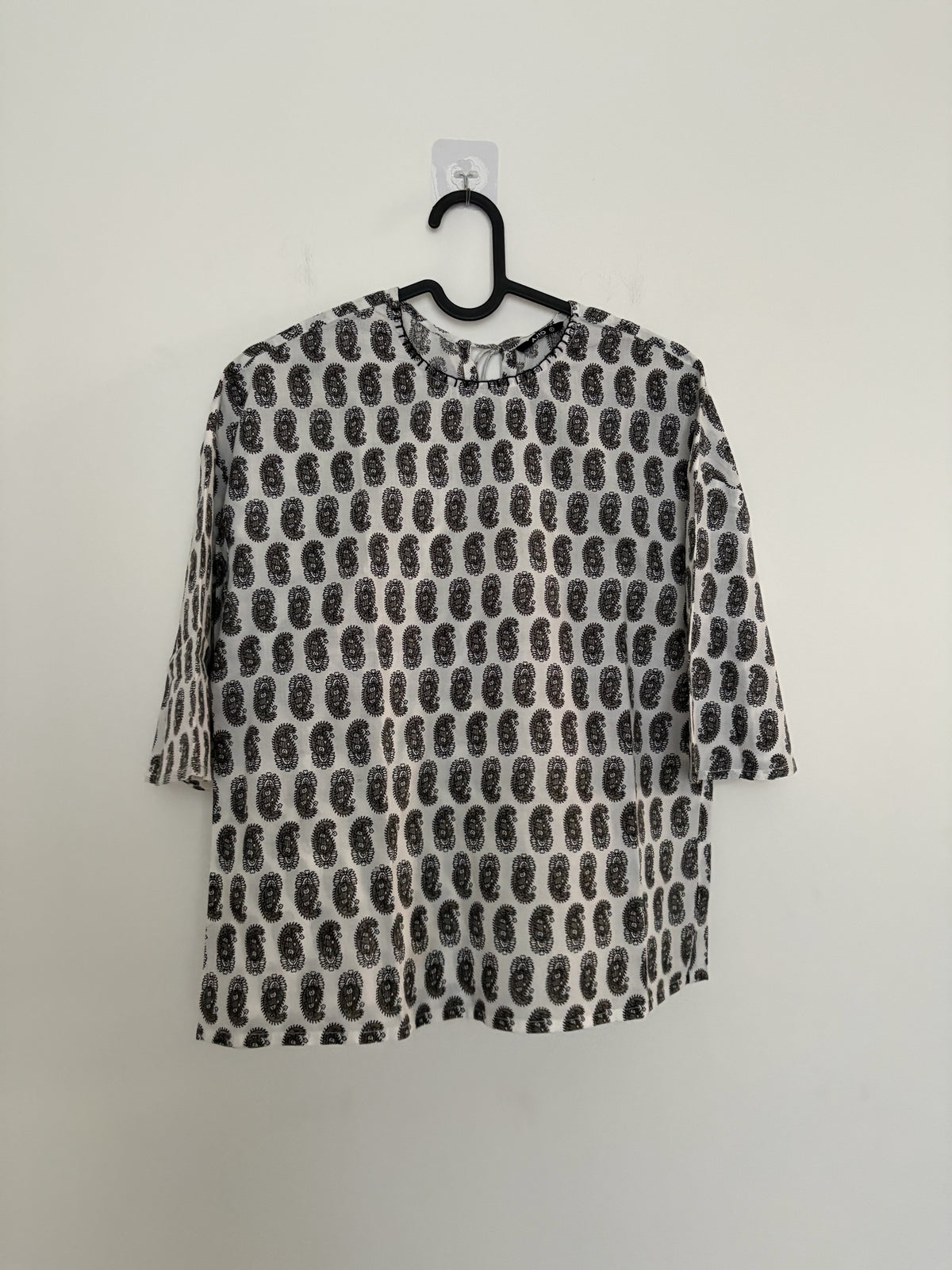 The Circle monochrome paisley print top with three-quarter sleeves, round neck, and relaxed boxy fit on a hanger