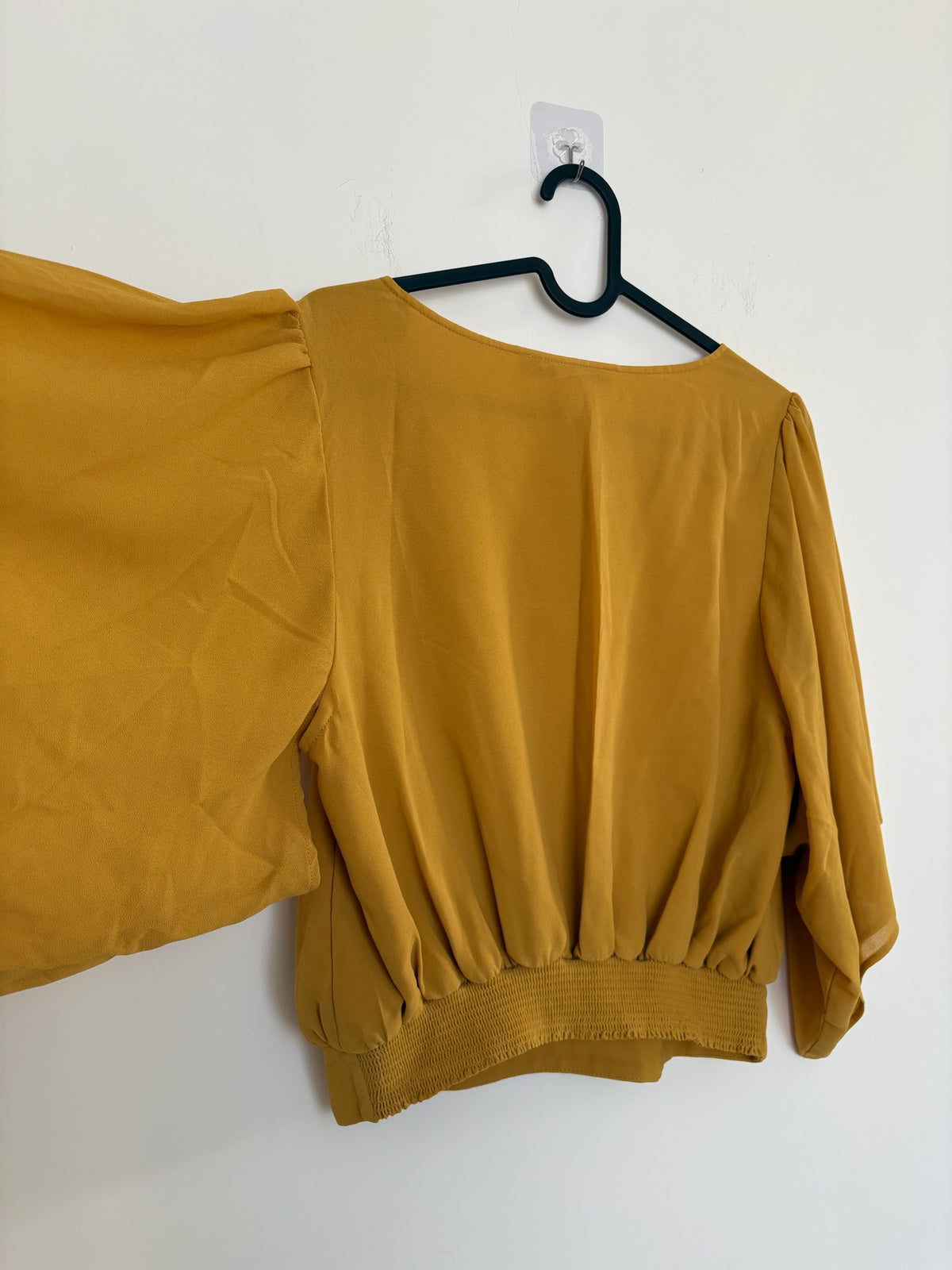 The Circle Forever 21 mustard yellow blouse with flowy flutter sleeves and a smocked back hem hanging on a hanger.