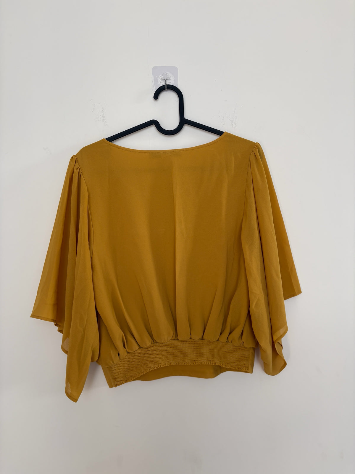 The Circle Forever 21 mustard yellow blouse featuring flowy flutter sleeves and a smocked back hem on a hanger.