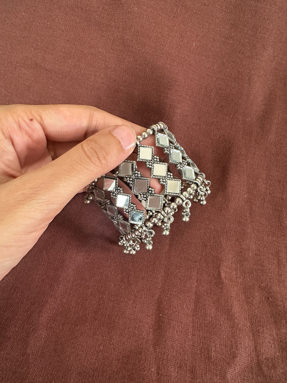 The Circle handcrafted oxidised silver cuff bracelet with square mirror work and dangling bead charms on brown fabric.