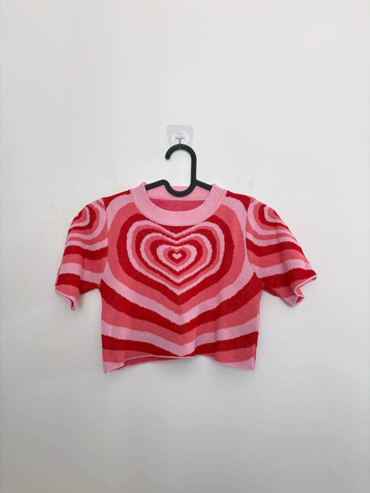 The Circle short sleeve knit crop top featuring a vibrant pink and red concentric heart pattern on a white background