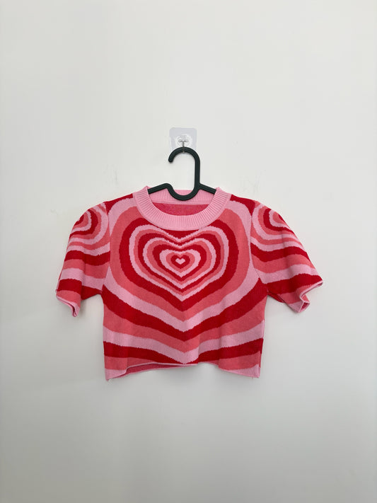 The Circle short sleeve knit crop top featuring a vibrant pink and red concentric heart pattern on a white background