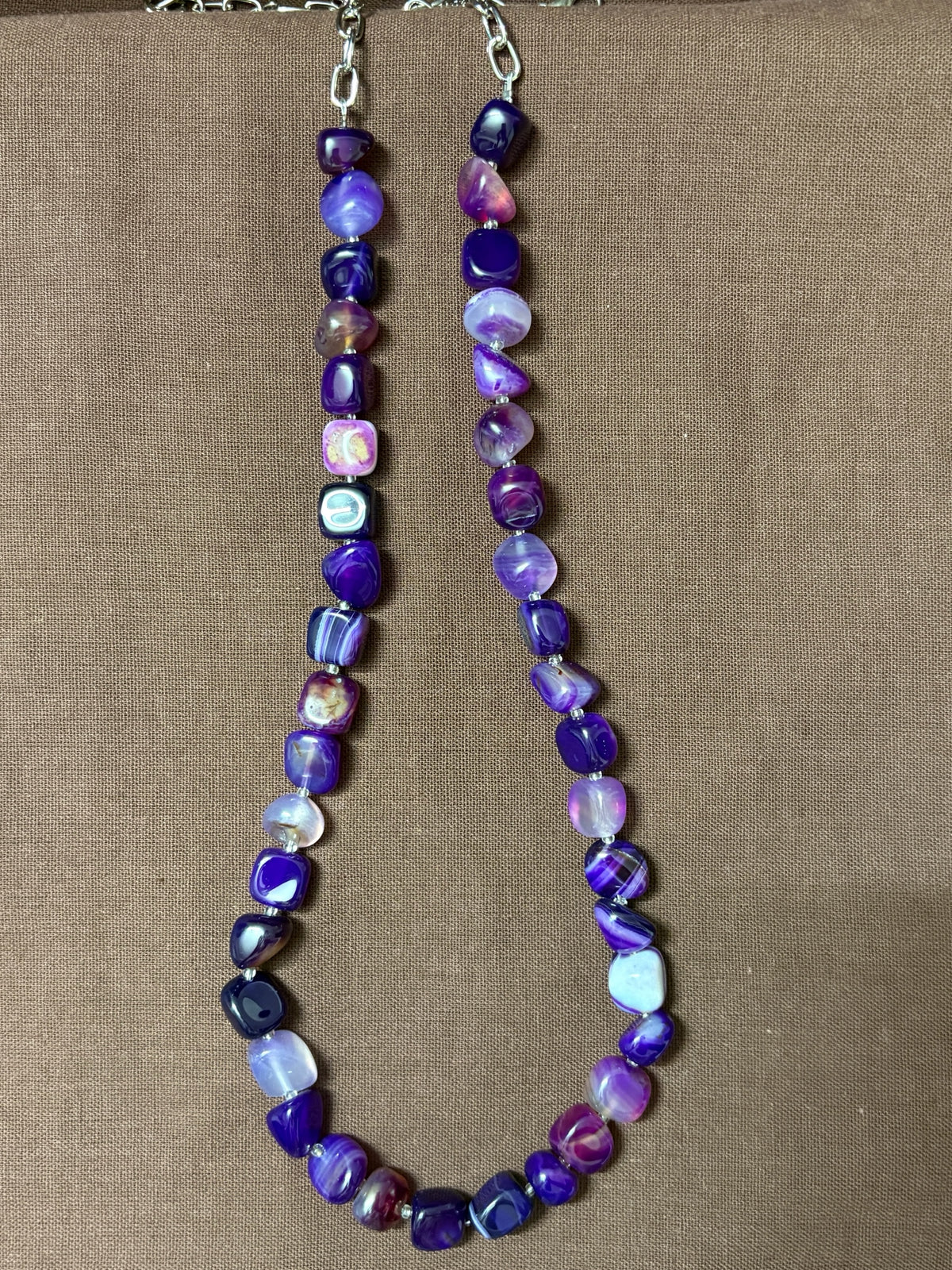 The Circle purple agate beaded necklace with smooth tumbled stones and a silver-tone clasp on a brown background.