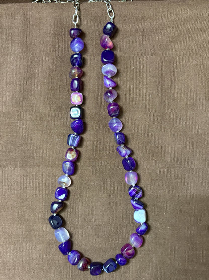 The Circle purple agate beaded necklace with smooth tumbled stones and a silver-tone clasp on a brown background.