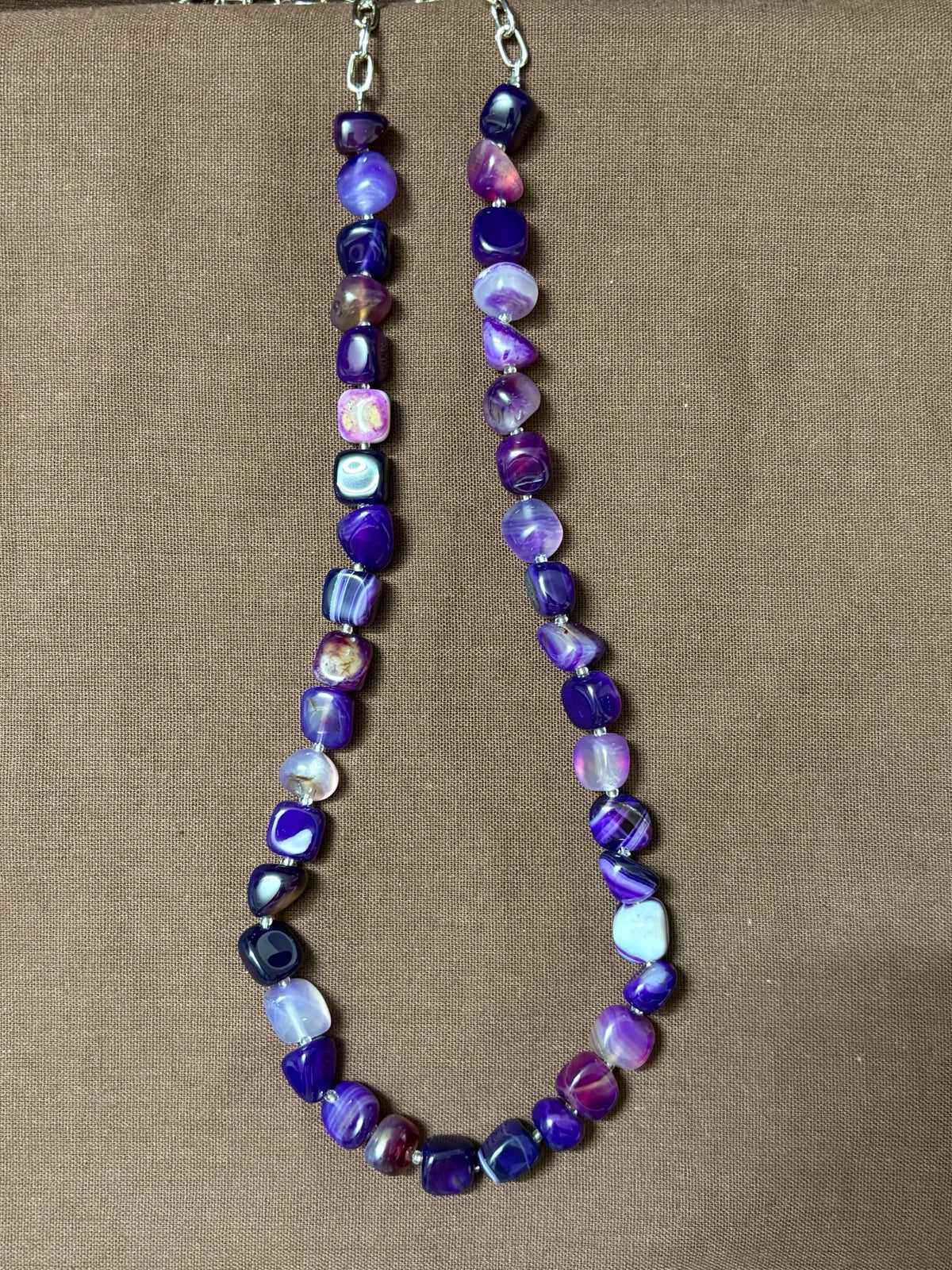 The Circle purple agate beaded necklace with smooth tumbled stones and a silver-tone clasp on a brown background.