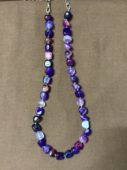 The Circle purple agate beaded necklace with smooth tumbled stones and a silver-tone clasp on a brown background.