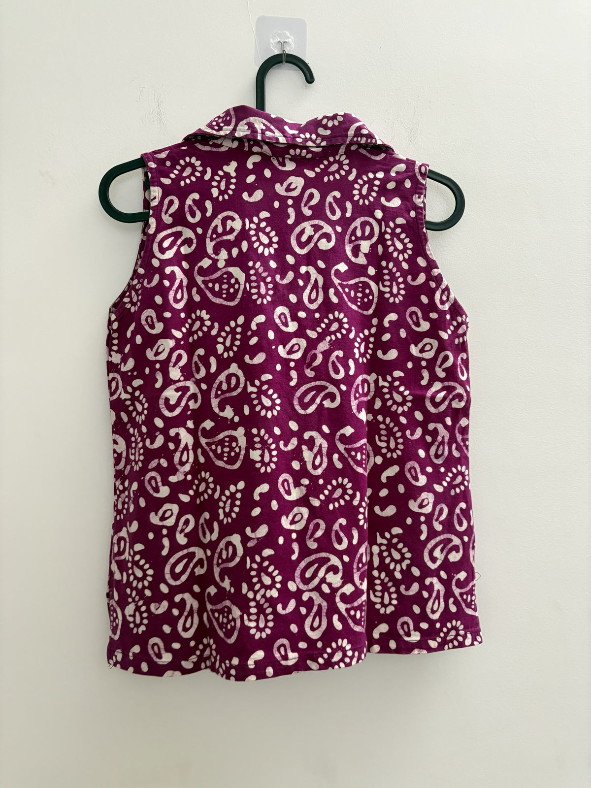 The Circle sleeveless polo top in deep purple with a white paisley batik print, hanging on a hanger.