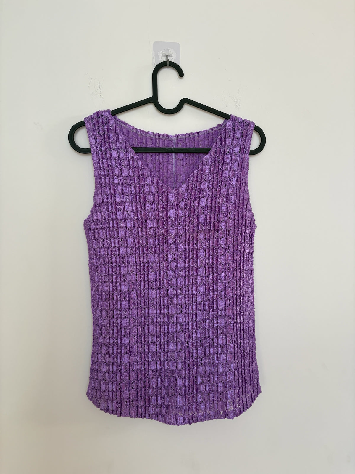 The Circle purple sleeveless V-neck top with a textured crinkle finish hanging on a black hanger against a white wall.