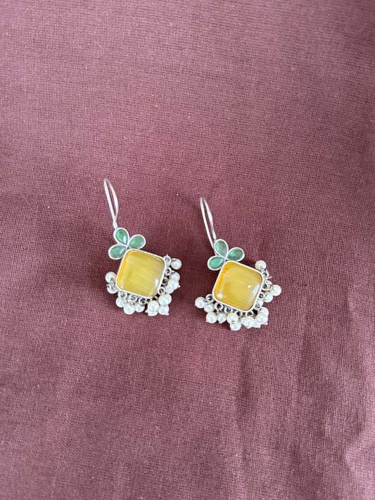 The Circle silver-toned drop earrings with square yellow stones, green floral accents, and dangling white pearl beads.
