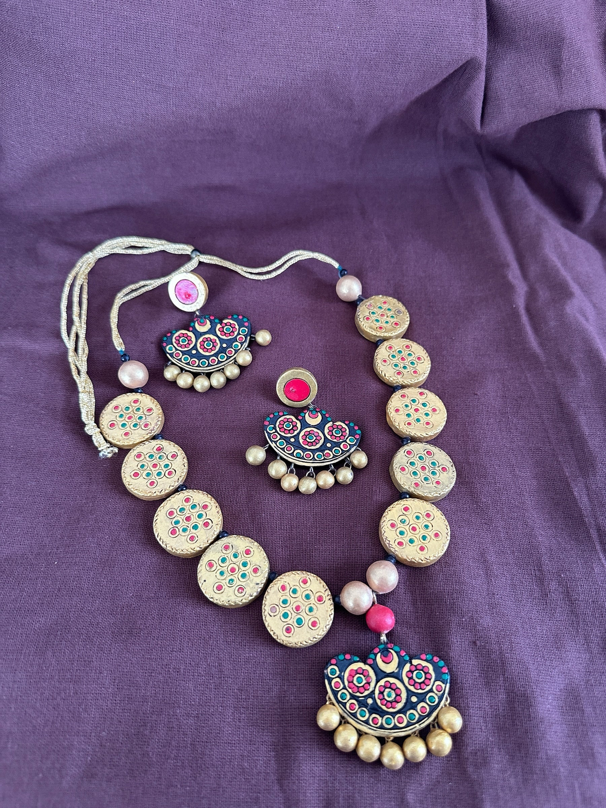 The Circle handcrafted terracotta necklace and earring set with gold circular motifs and pink, teal, and red accents.