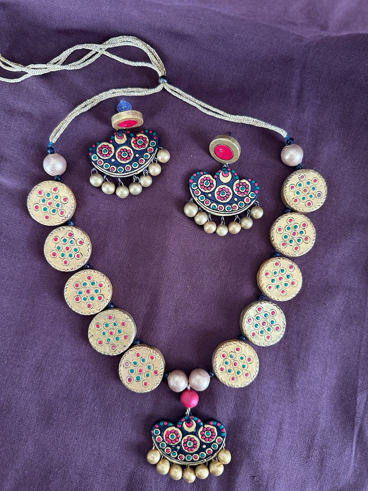 The Circle handcrafted terracotta necklace and earring set with gold circular motifs, pink, teal, and red accents.