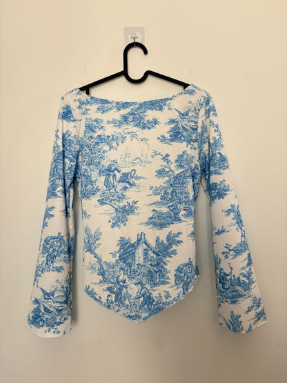 The Circle blue and white toile print long sleeve top with a sweetheart neckline and flared sleeves on a hanger.
