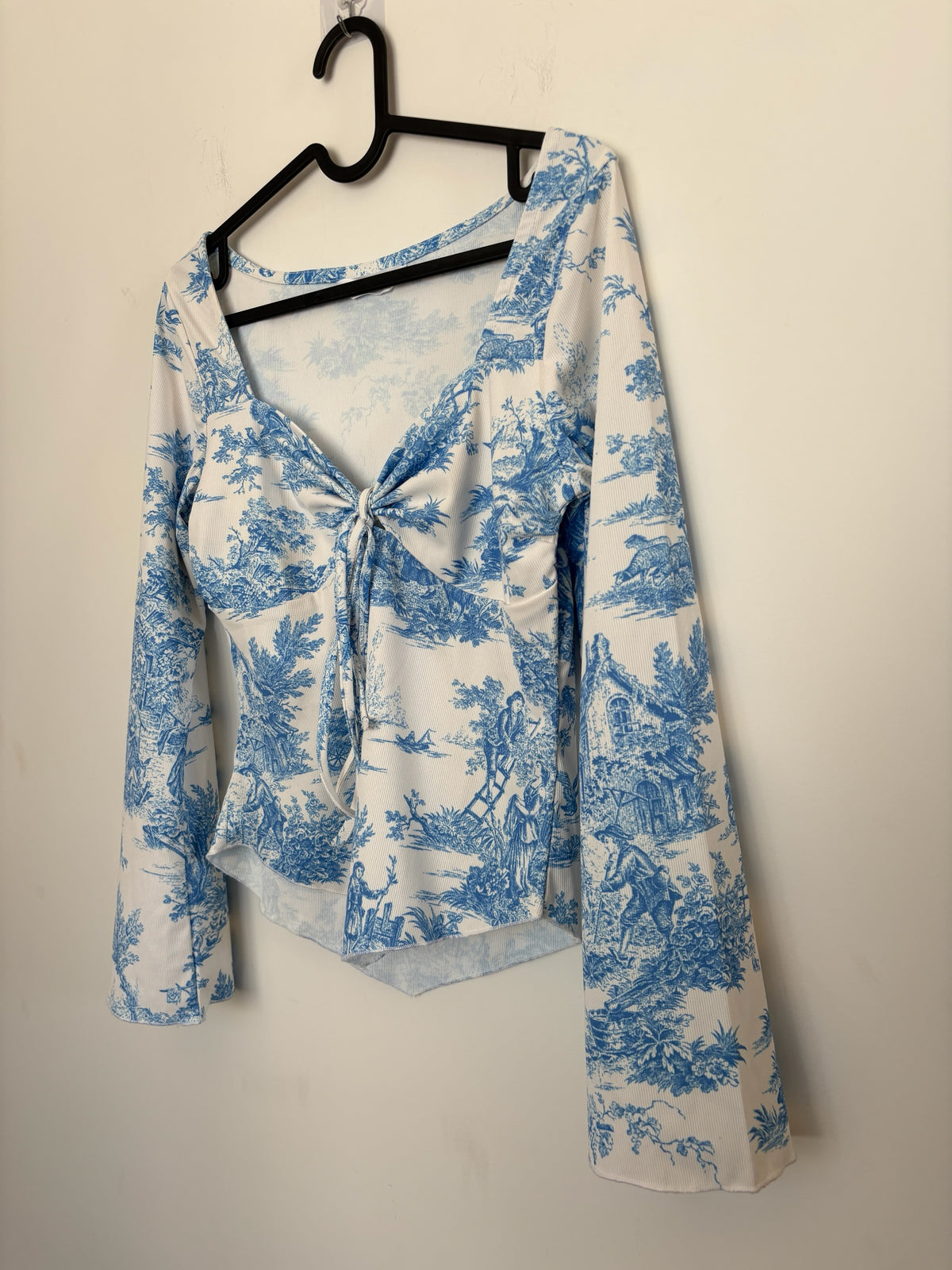 The Circle blue and white toile print long sleeve top with a sweetheart neckline and front tie detail on a hanger.
