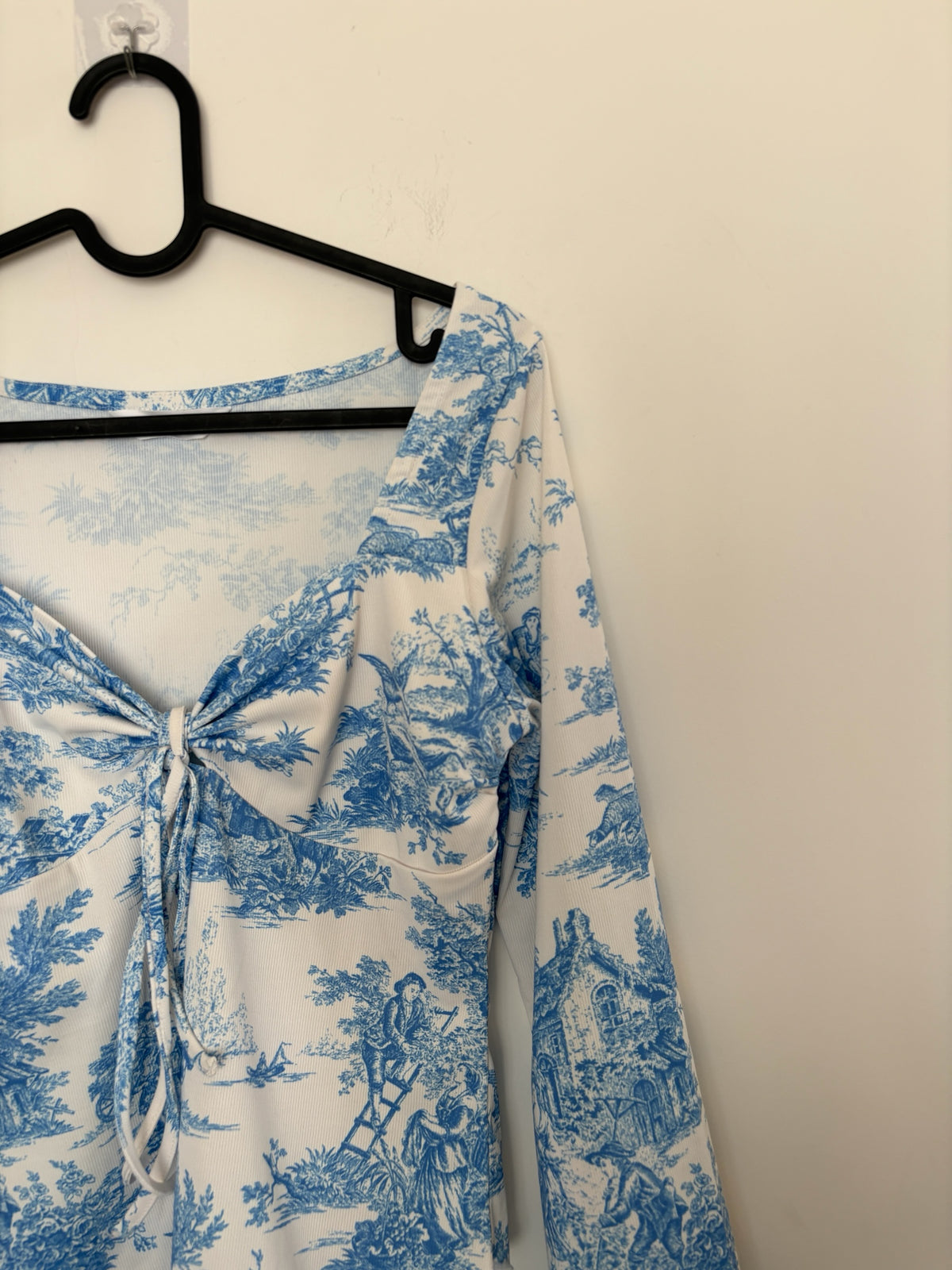 The Circle blue and white toile print long sleeve top with a sweetheart neckline and front tie detail on a hanger.