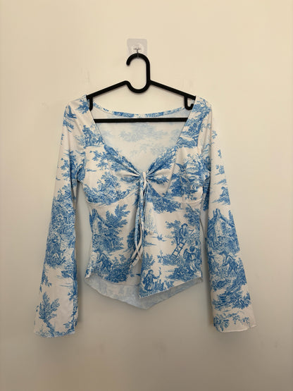 The Circle blue and white toile print long sleeve top with a sweetheart neckline and front tie detail on a hanger.
