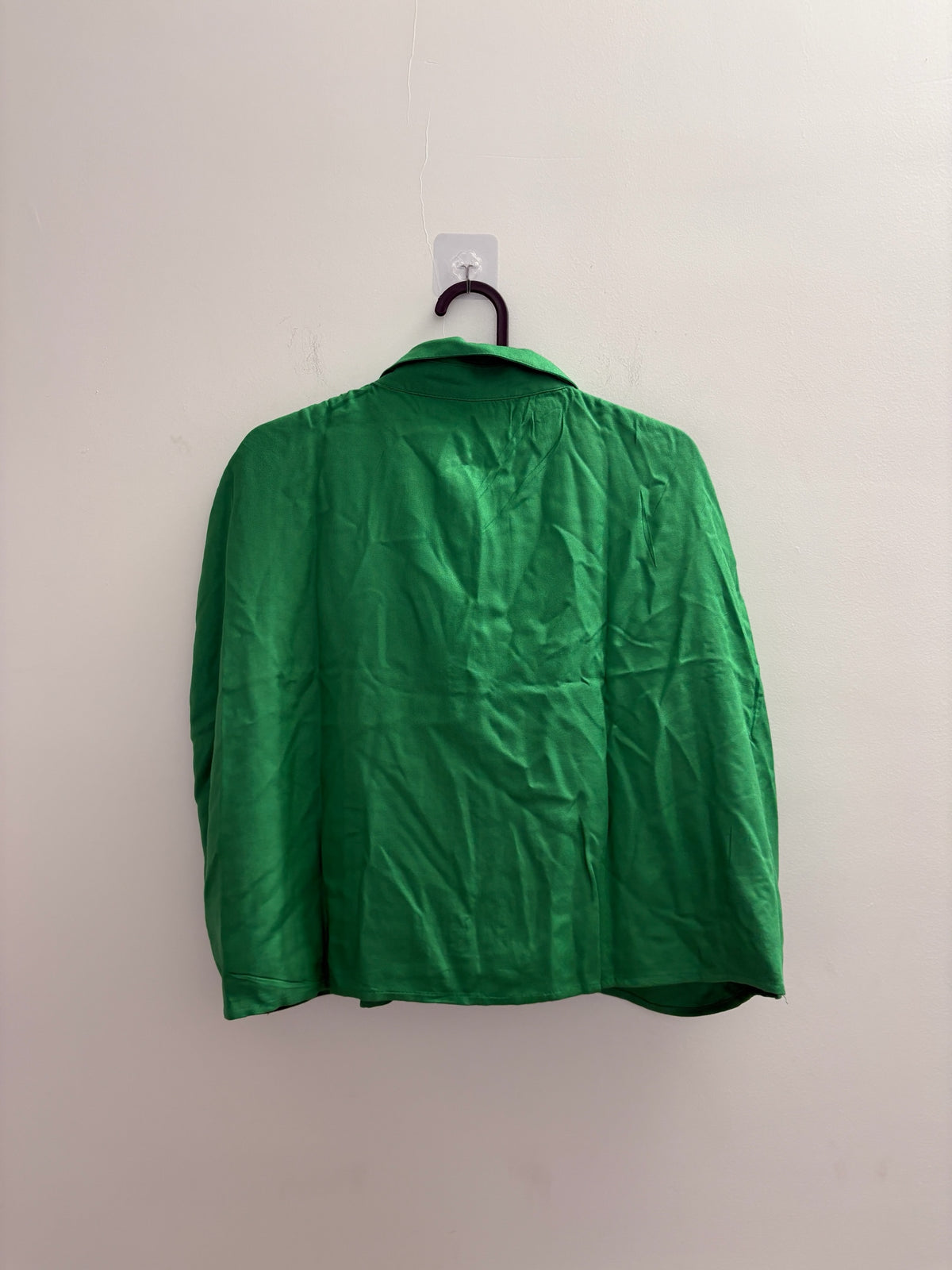 The Circle ZUDIO emerald green sleeveless button-down shirt with a classic collar hanging against a white wall.